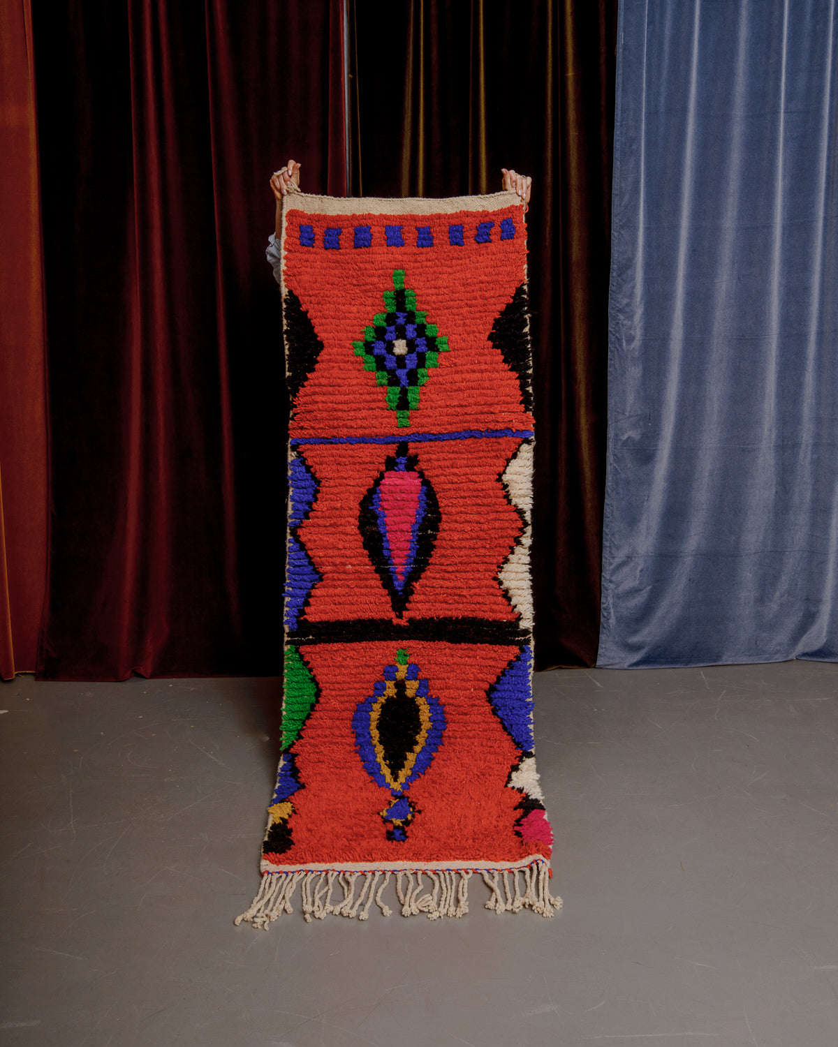 Vintage Berberlin boujaad runner rug being held up in front of velvet curtains.