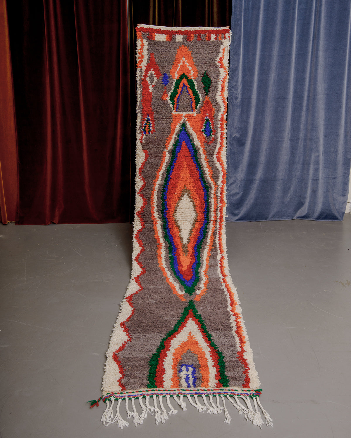 Vintage Berberlin boujaad runner rug being held up in front of a velvet curtains.