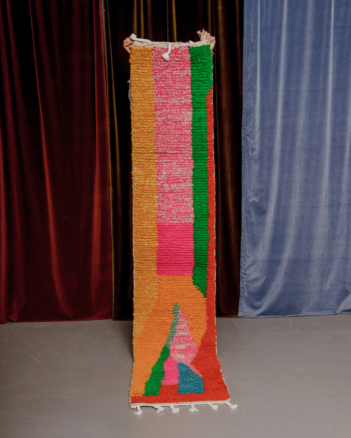 Vintage Berberlin boujaad runner rug being held up in front of velvet curtains.