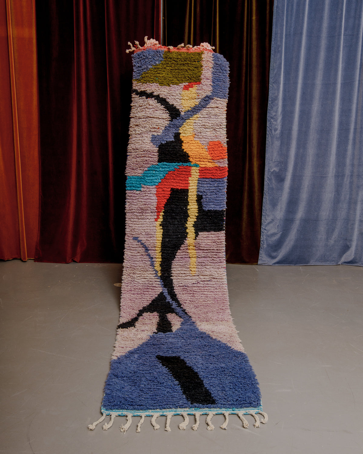 Vintage Berberlin boujaad runner rug being held up in front of a velvet curtains.