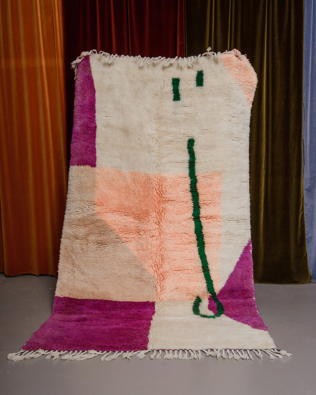 Berberlin Finest beniourain rug held in front of velvet curtains. 