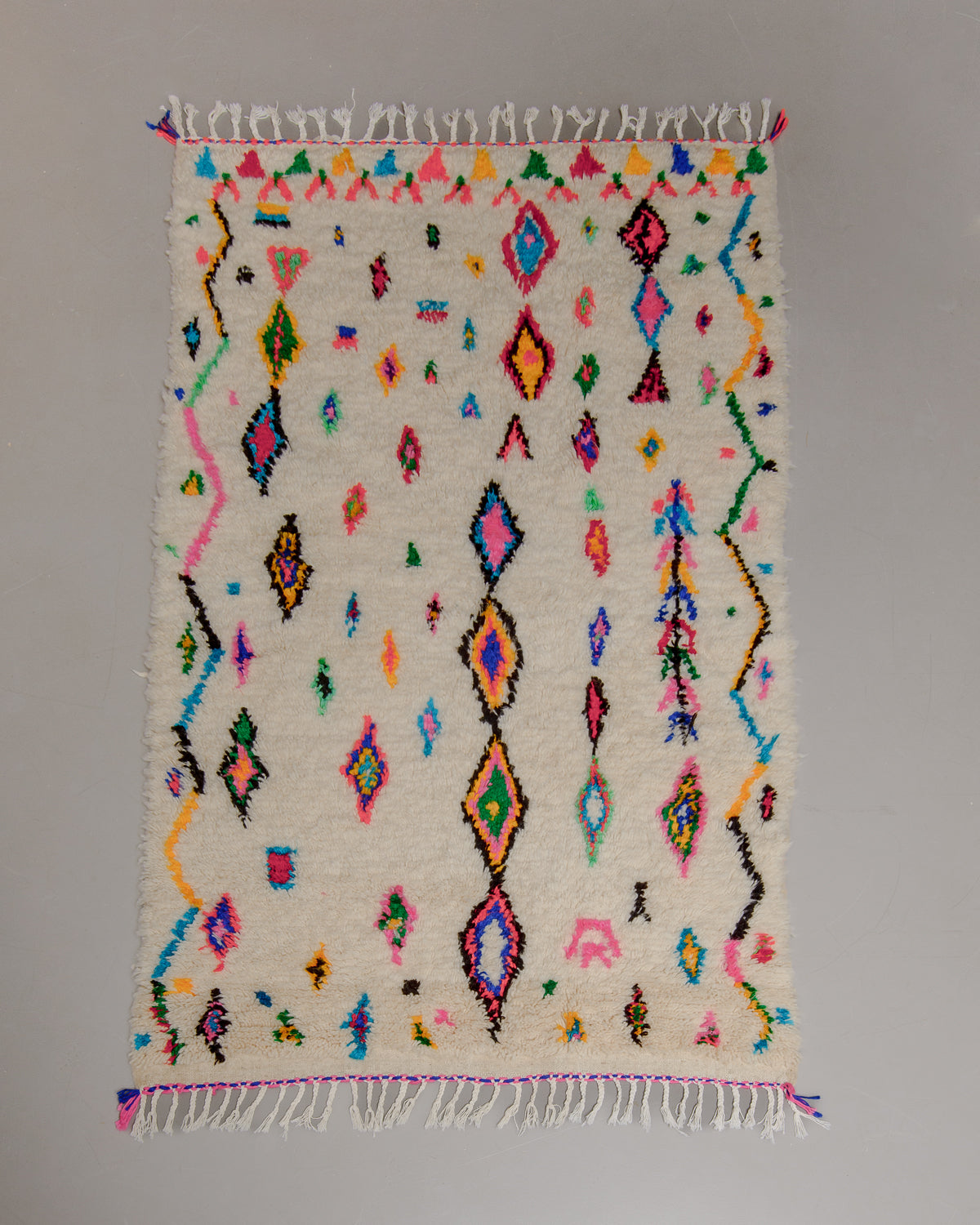 Azilal rug with colourful, abstract design laid flat on grey floor.