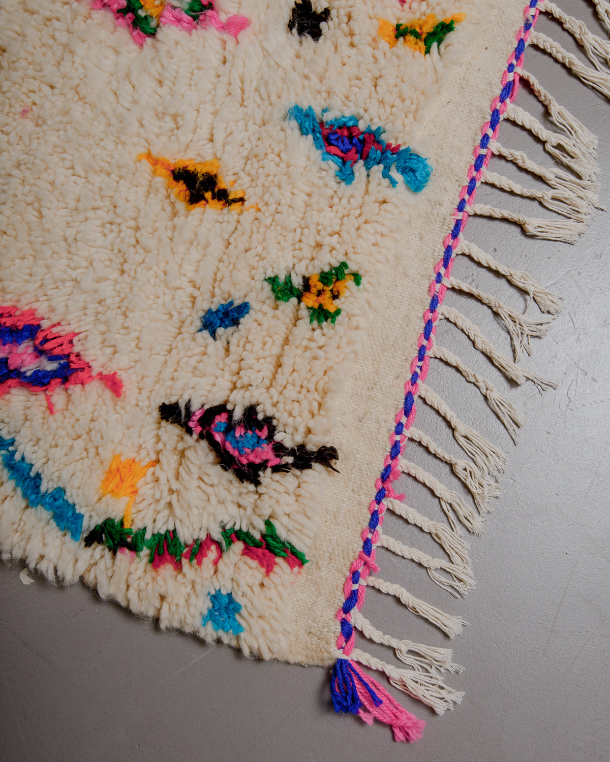 Corner of azilal rug with white cotton tassels and pink and blue edge.