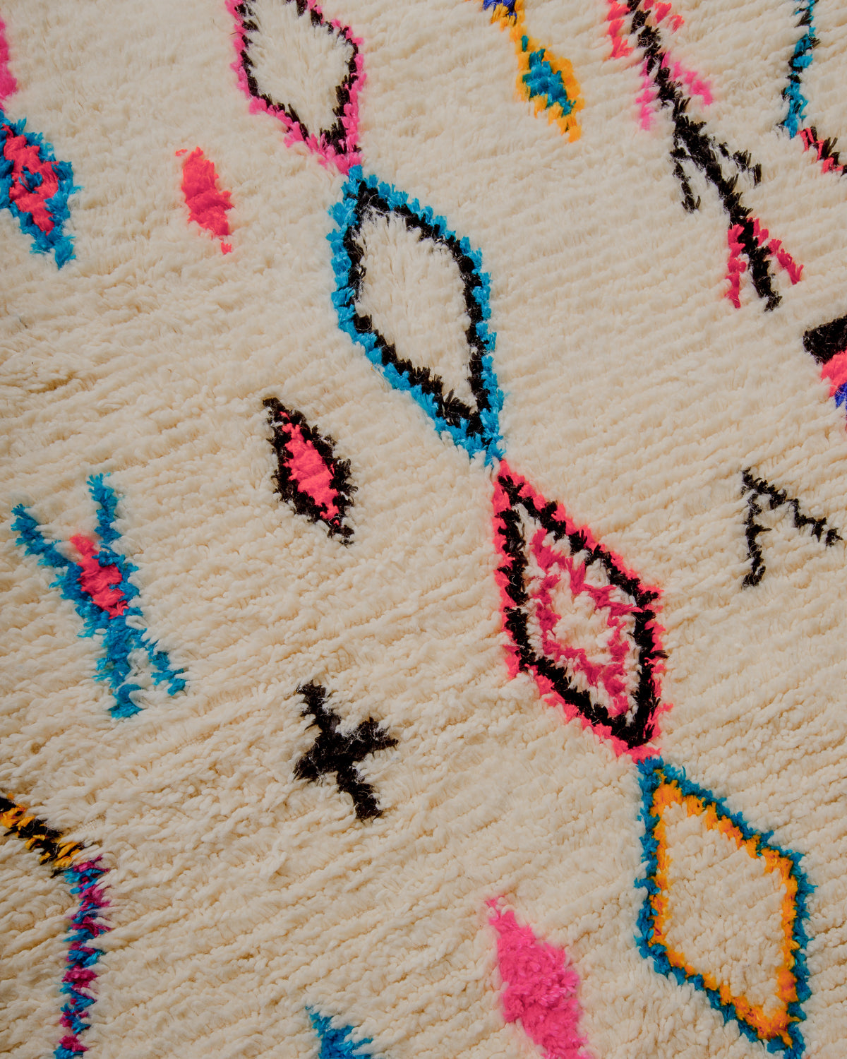 Surface of cream wool rug with symbols and motifs  in pink, black, blue and yellow.