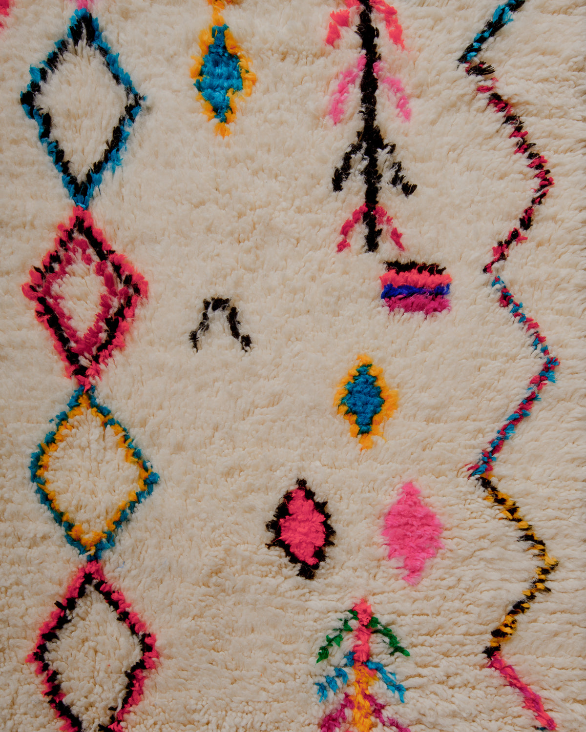 Surface of wool rug with colourful symbols on cream base.