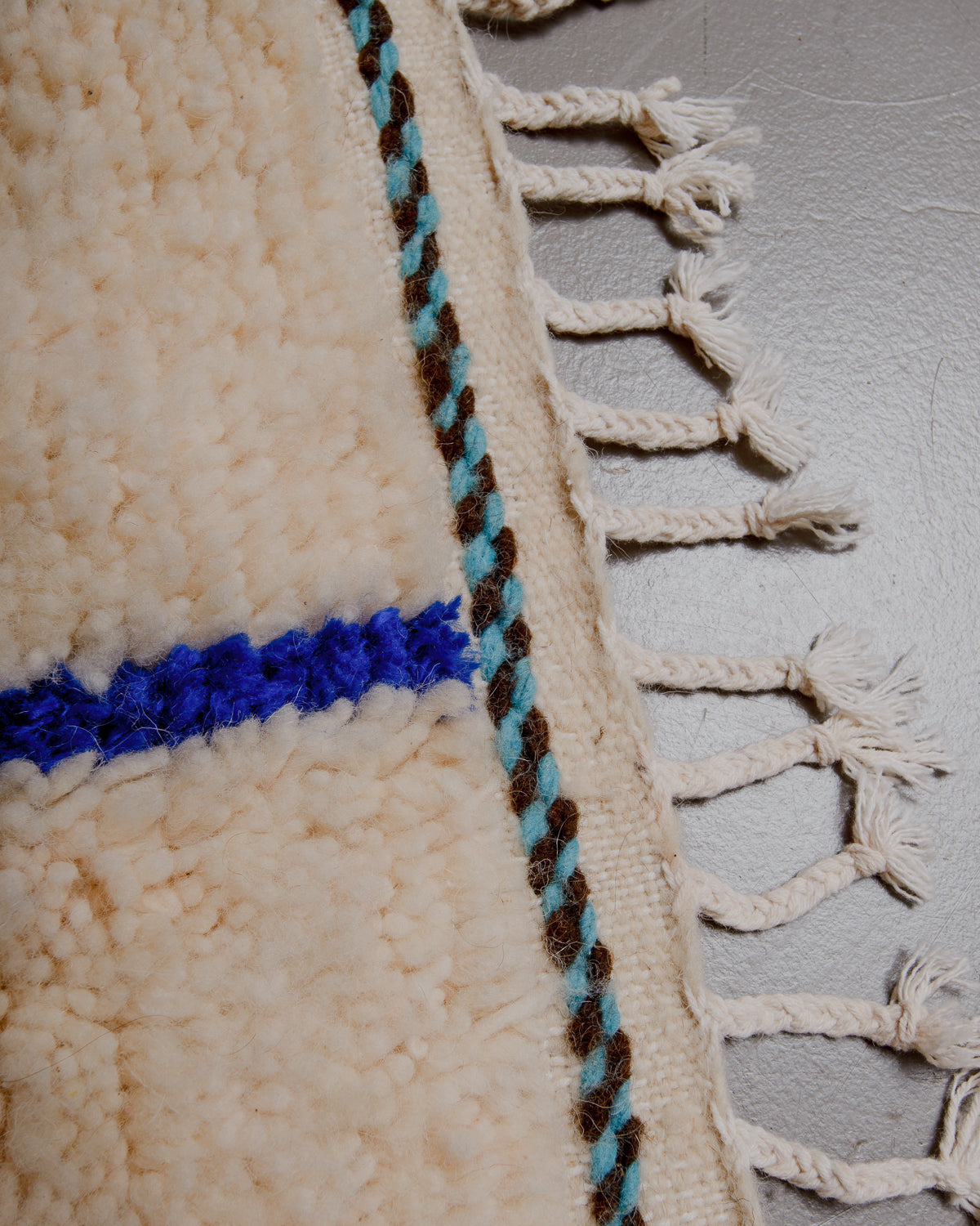 Close up of turquoise and brown embroidered line along the woven edge.