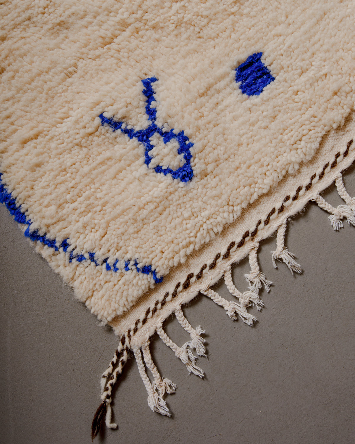 Corner of azilal rug with white cotton tassels and cream and brown embroidery along edge.