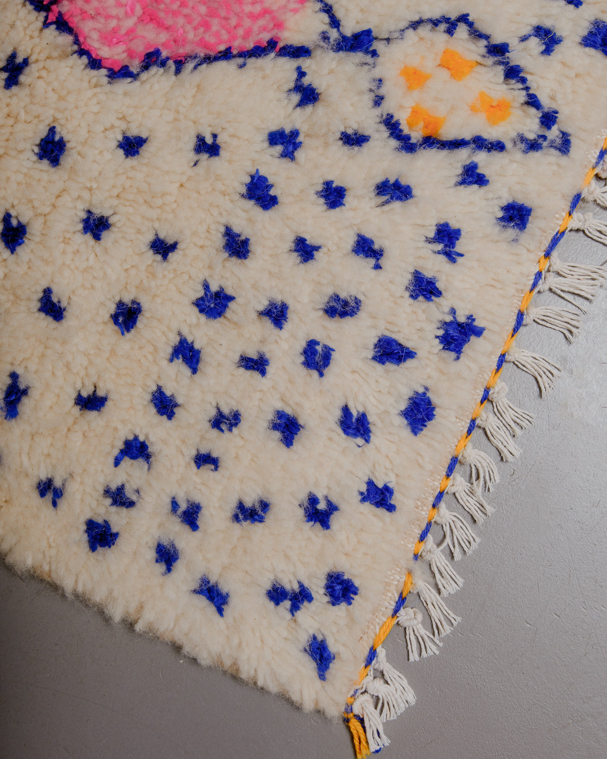 Corner of Berberlin Azilal rug with white cotton tassels and pink, blue and yellow accents.