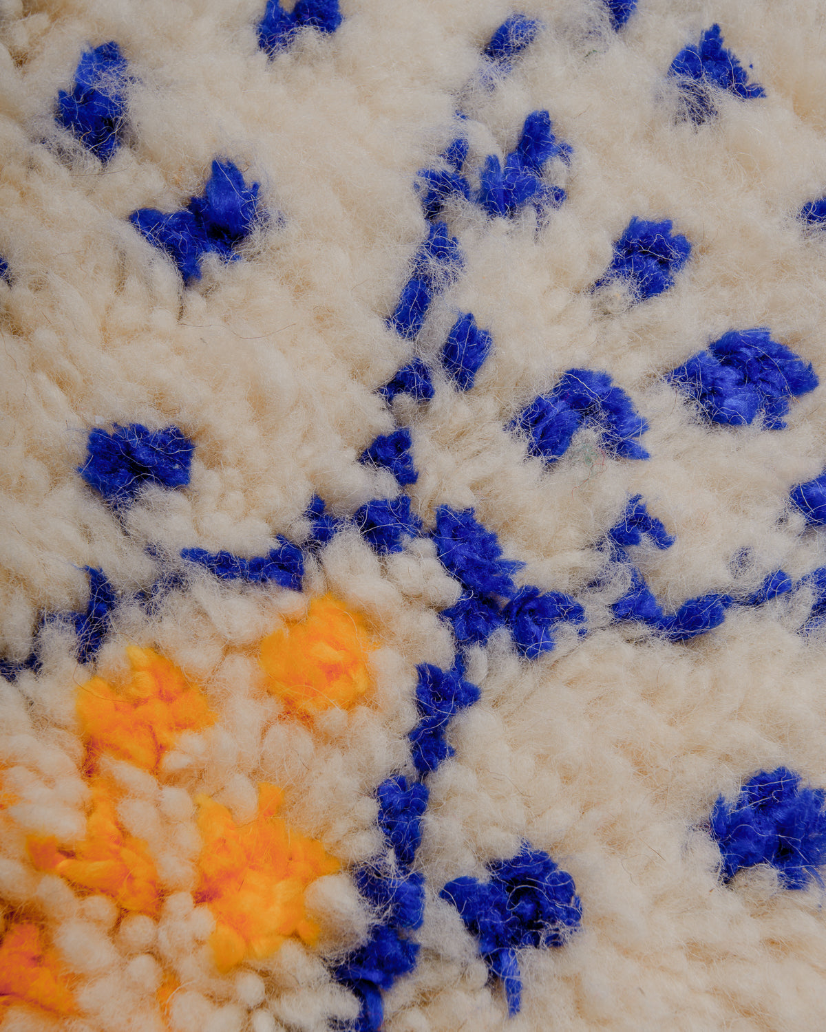 Surface of rug with cream wool and colourful lines and dots in blue and yellow cotton.