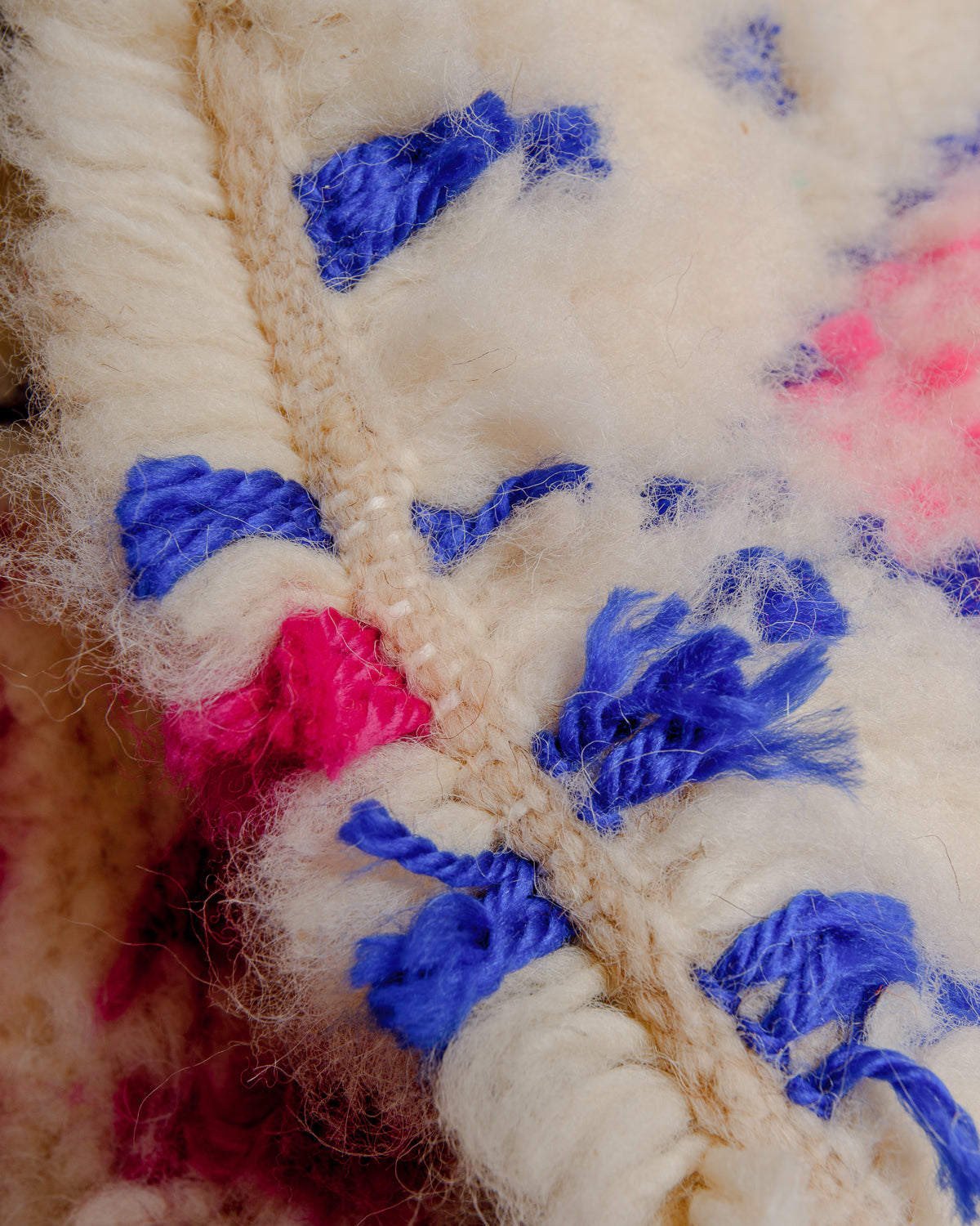 Close up of cream wool rug with colourful cotton details. 