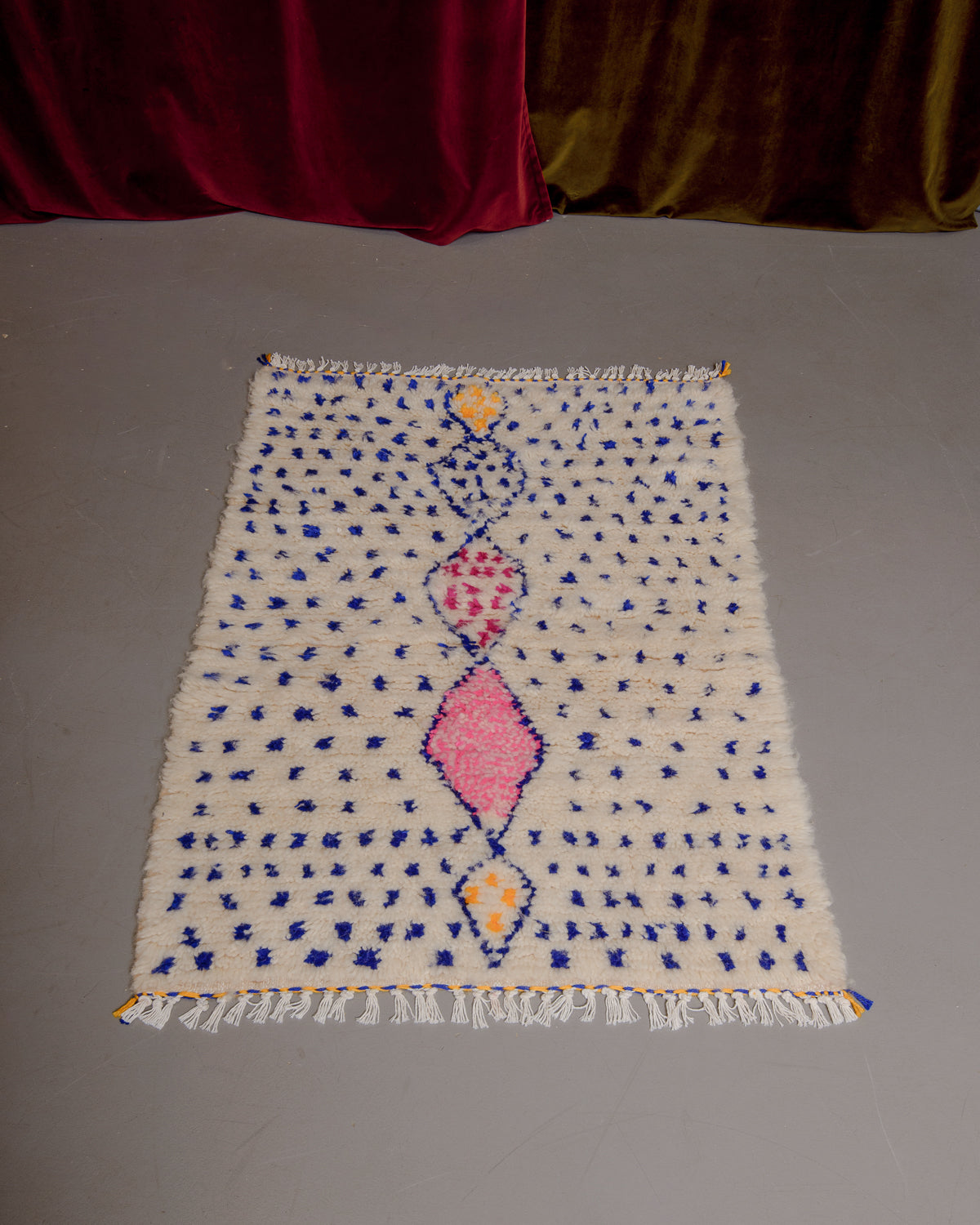 Small Berberlin Azilal rug on grey floor in front of a velvet curtain.