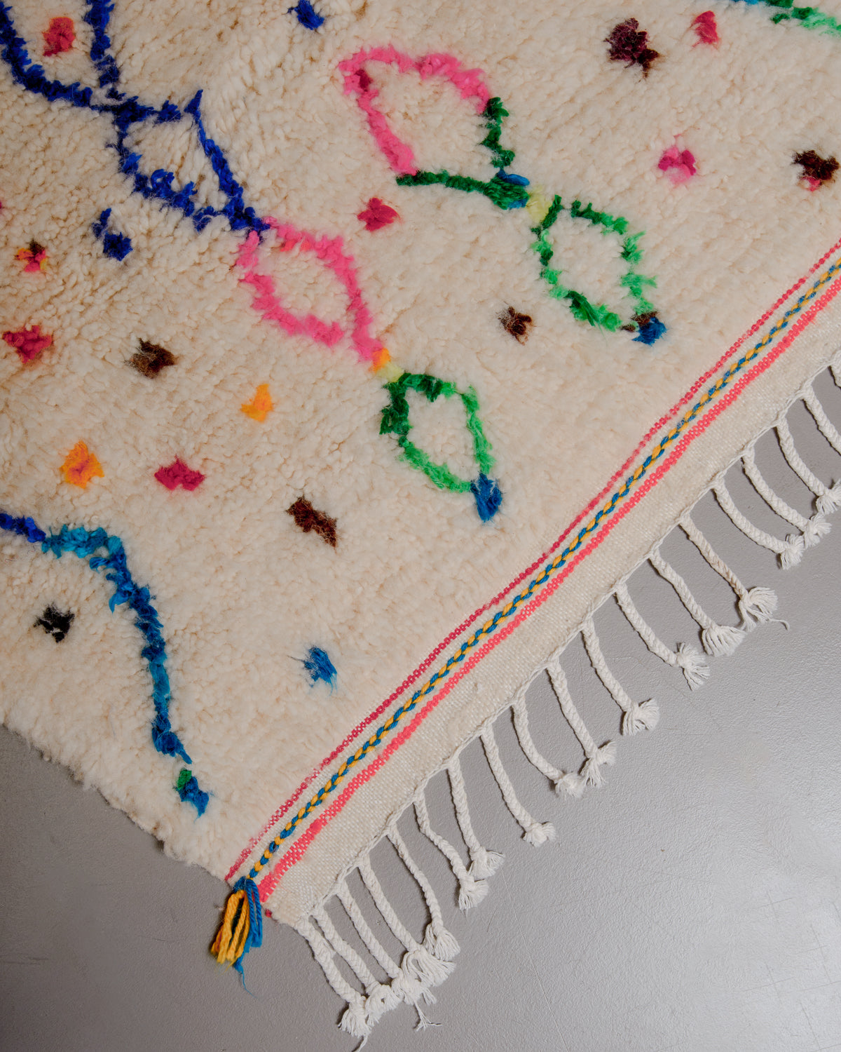 Corner of Berberlin Azilal rug with white cotton tassels and colourful lines across the woven edge.