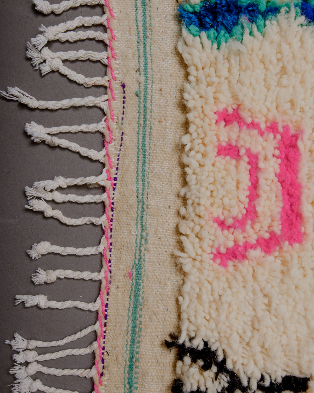 Edge of rug with white cotton tassels and turquoise and pink woven into the edge.