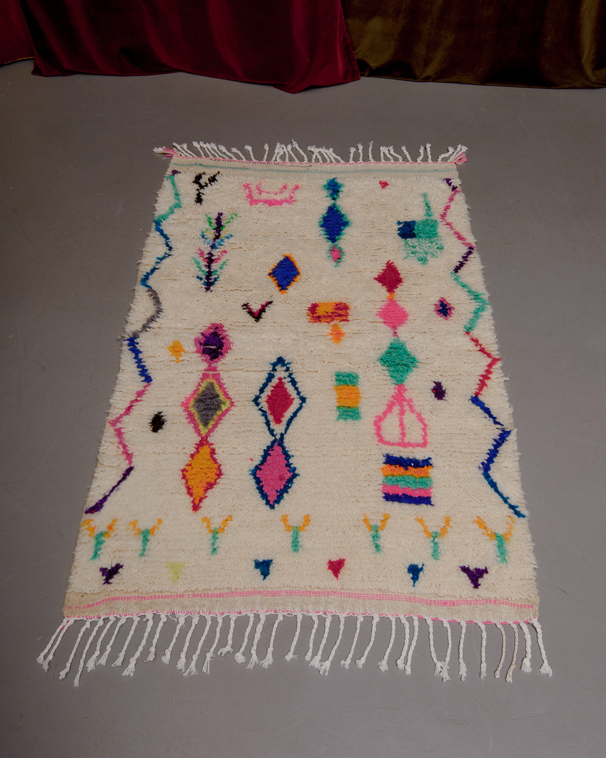Small Berberlin Azilal rug on grey floor in front of velvet curtains.