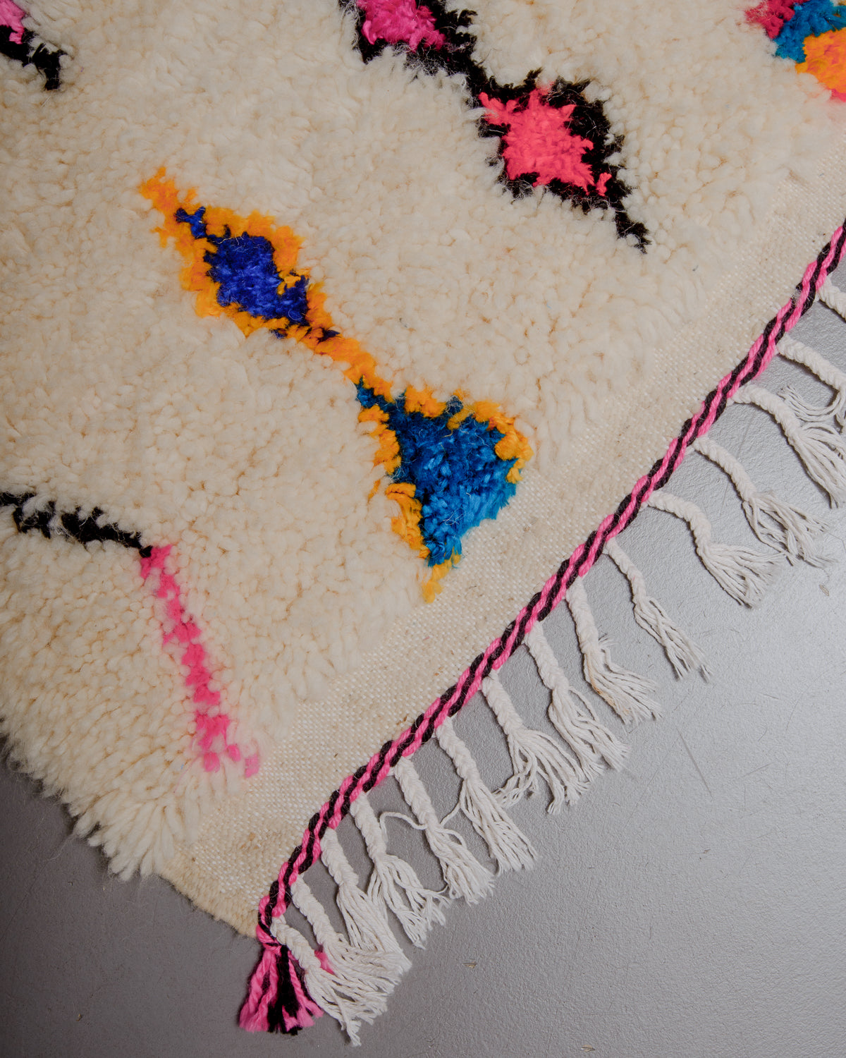 Corner of rug with white cotton tassels and black and pink woven across the edge.