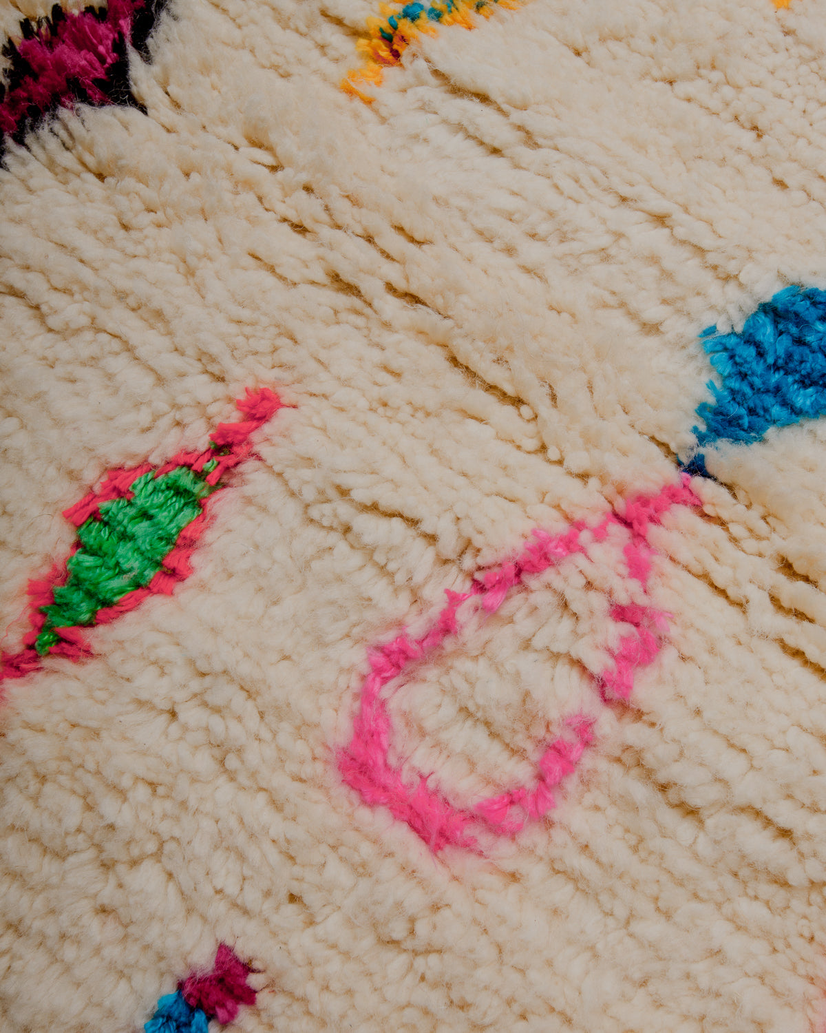 Surface of rug with cream wool base and colourful pattern of symbols and lines in dyed cotton.