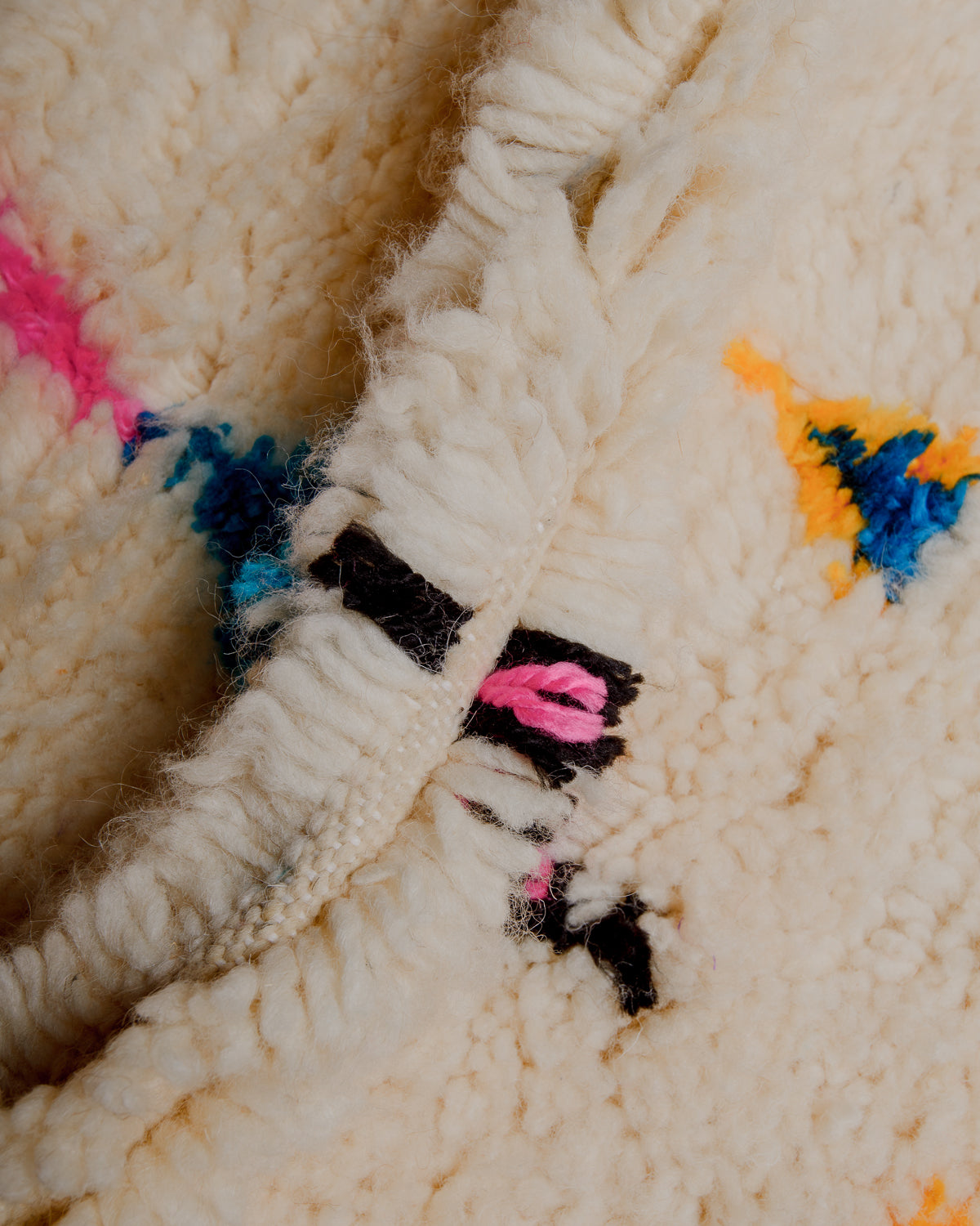 Close up of cream wool rug with colourful details in wool and cotton.