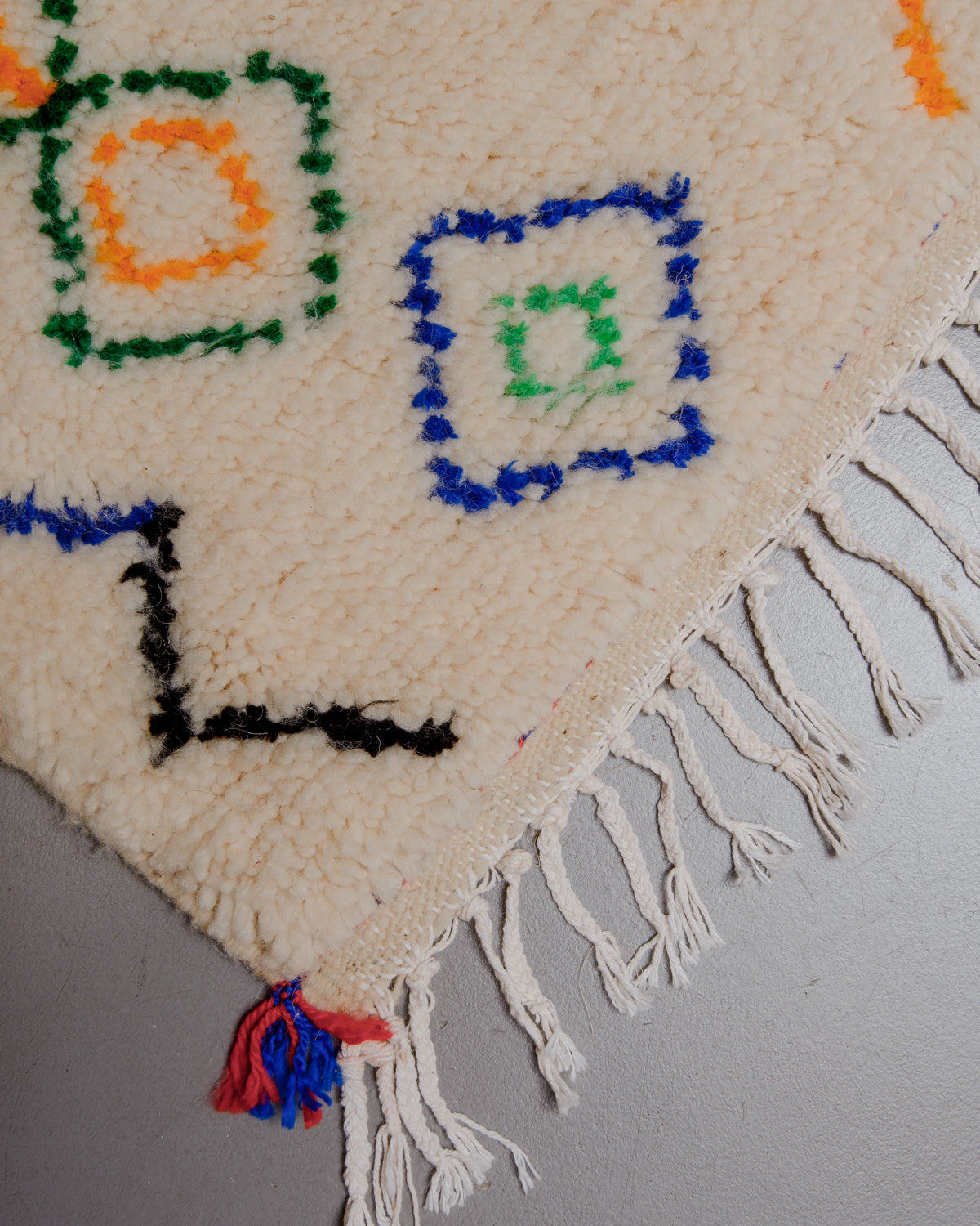 Corner of rug with white cotton tassels across the edge.
