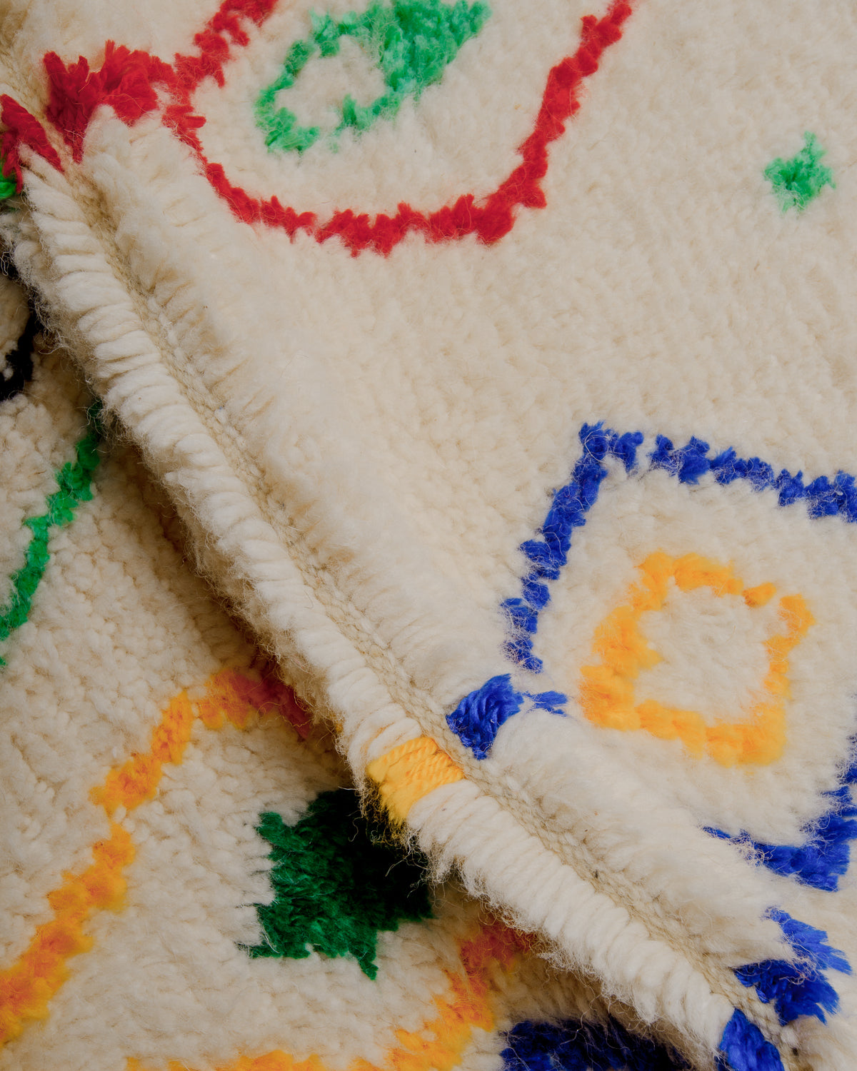 Close up of cream wool rug with colourful details in cotton.