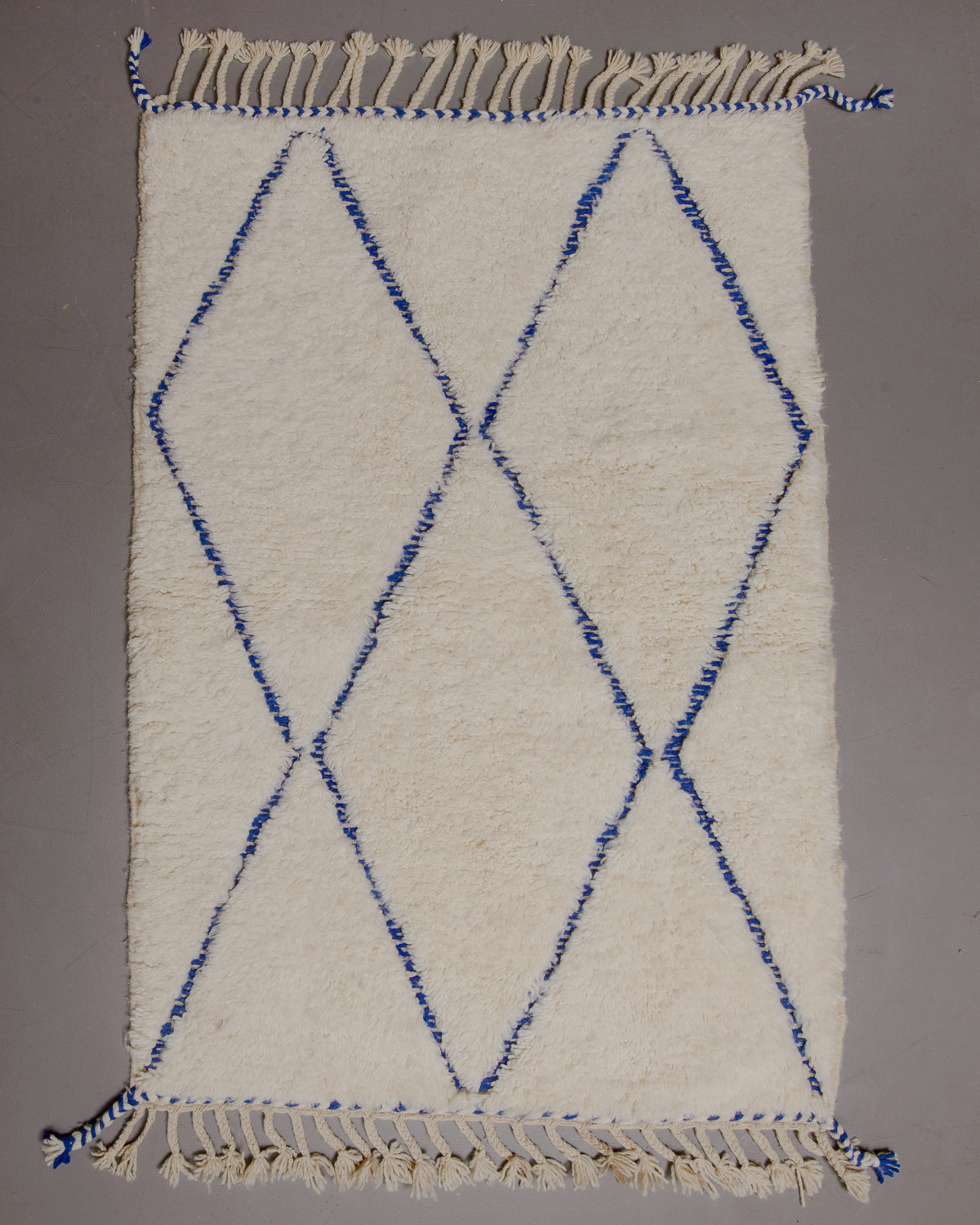 Berberlin Beniourain rug with blue diamond pattern on grey floor.