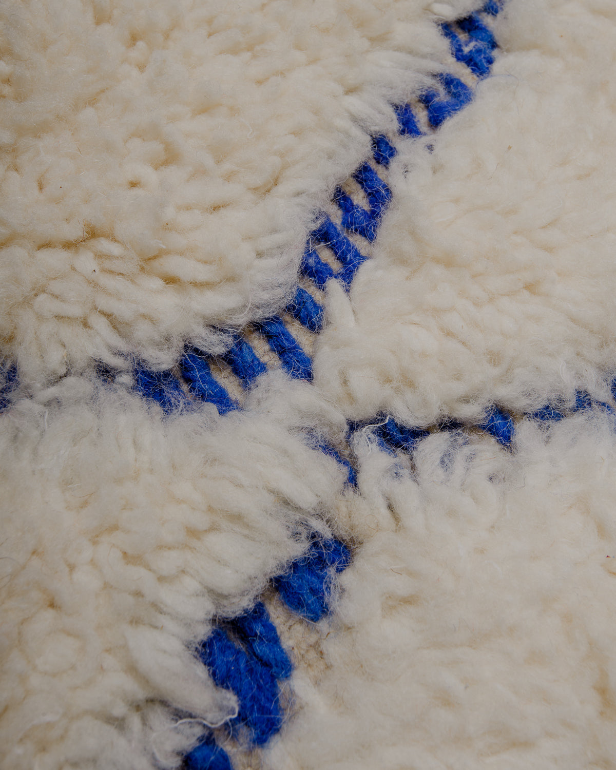 Close up of cream wool rug with blue embroidered design elements.