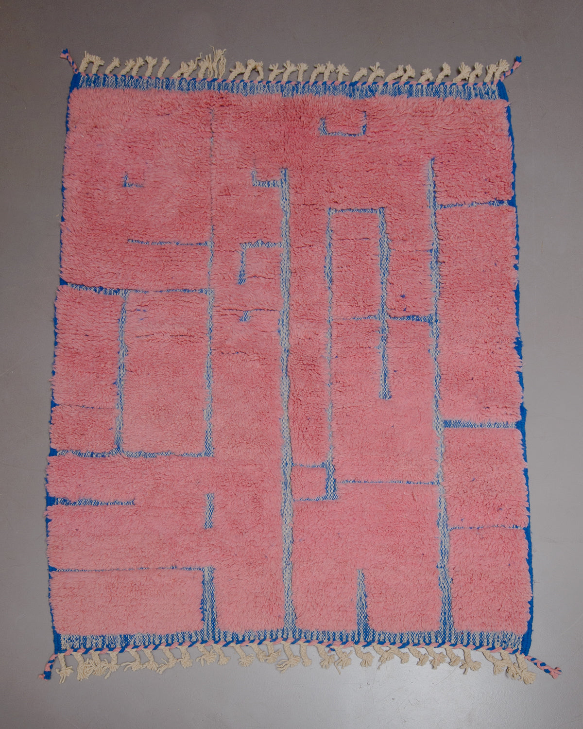 Beniourain rug in pink and blue wool on grey floor. 