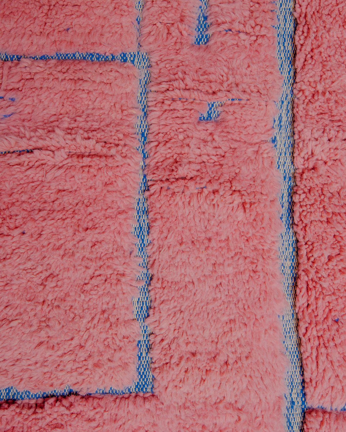 Surface of wool rug with a combination of fluffy pink pile and flat woven areas in blue.