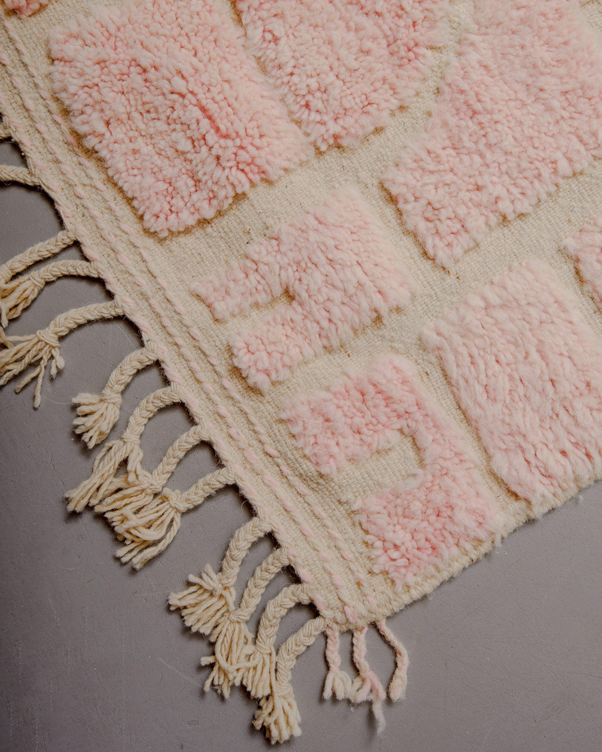 Corner of rug with wool tassels and a flat woven edge.