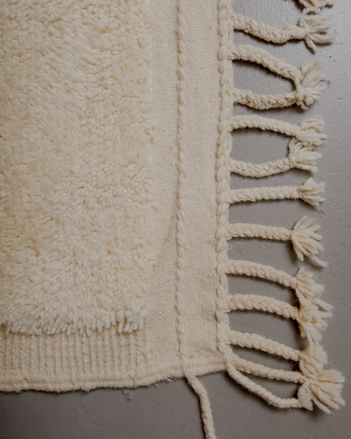 Corner of rug with wool tassels and a flat woven edge.