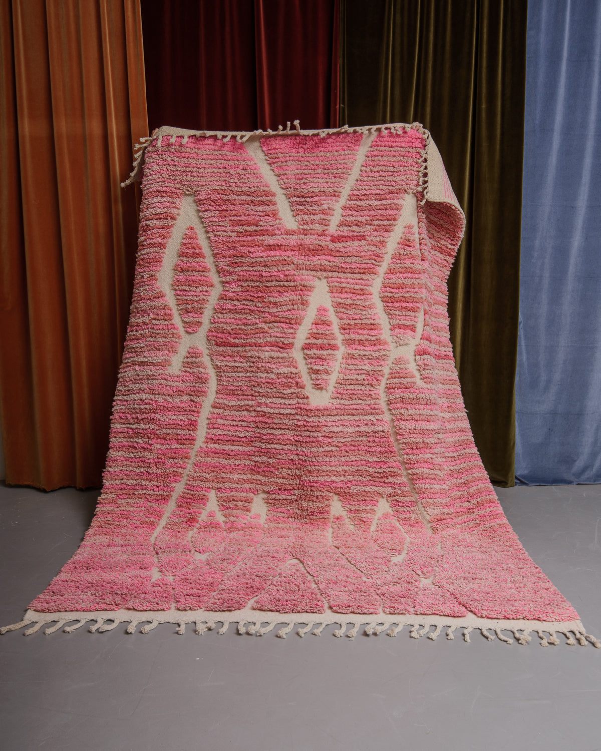 Berberlin Boujaad rug in different shades of pink wool with organic woven lines being held in front of velvet curtains.