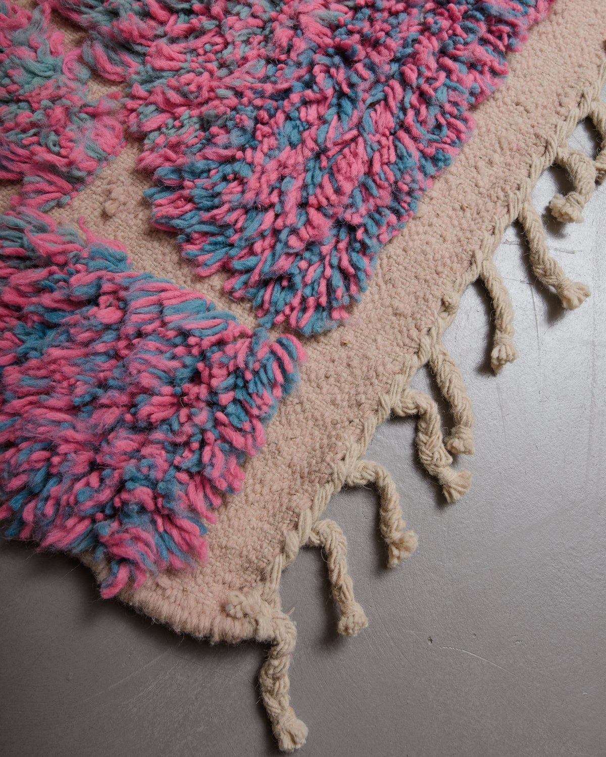 Corner of vintage wool rug with textured pile and flat woven edge with natural wool tassels. 