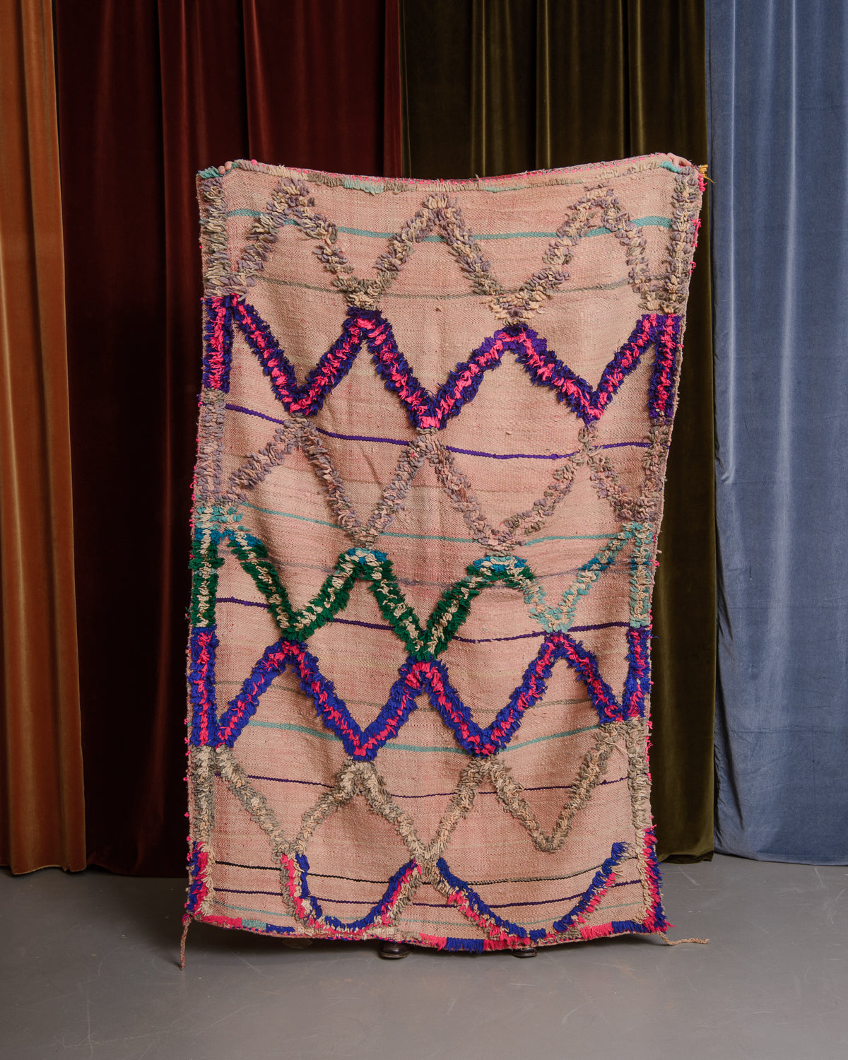 Vintage flat woven Kelim with fluffy embroidered pattern, held in front of velvet curtains. 