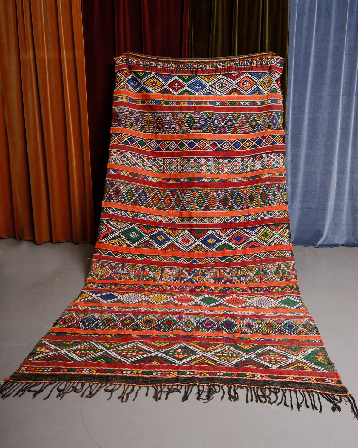 Colourful Vintage Kelim being held in front of velvet curtains. 