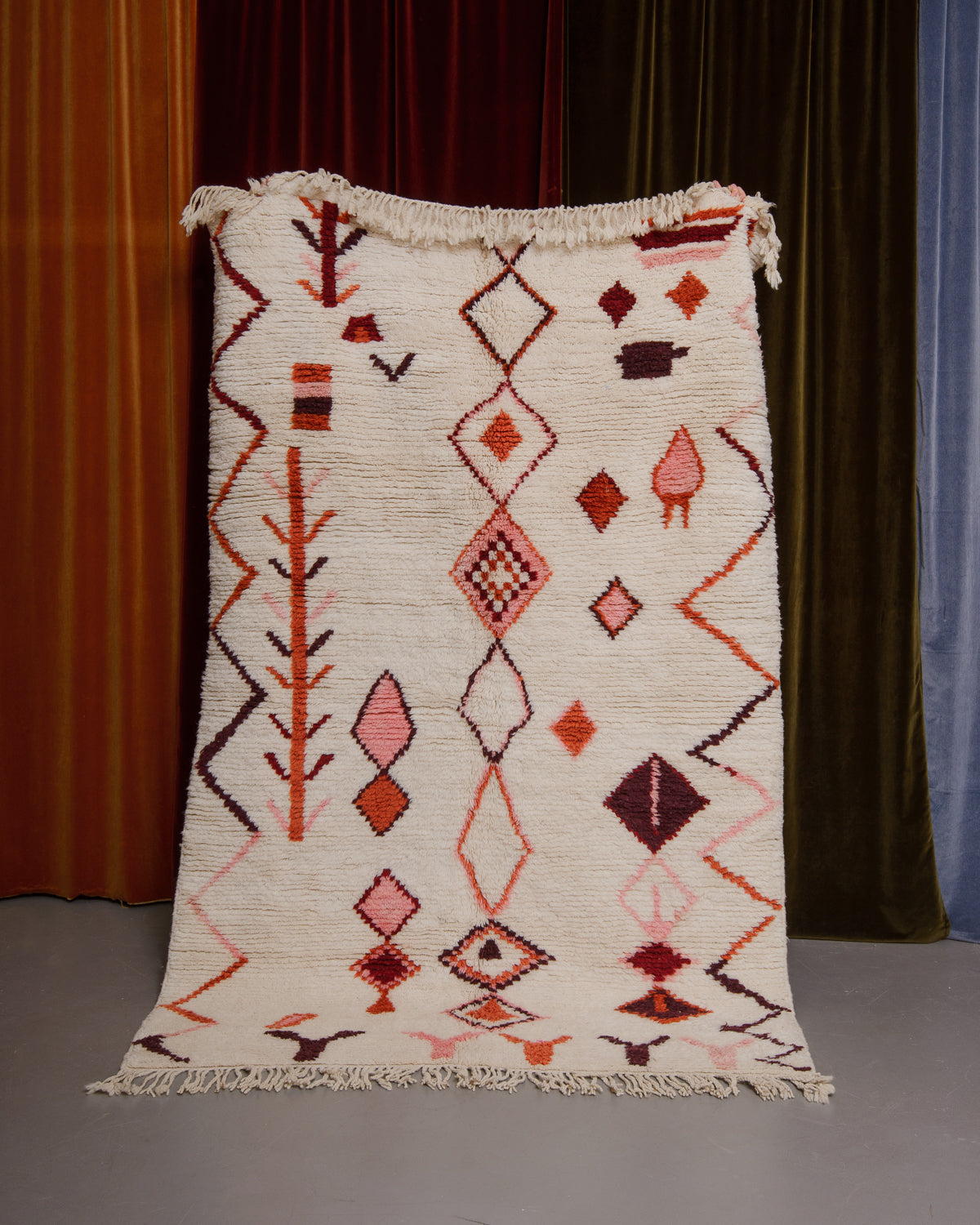 Azilal rug held in front of velvet curtains. 
