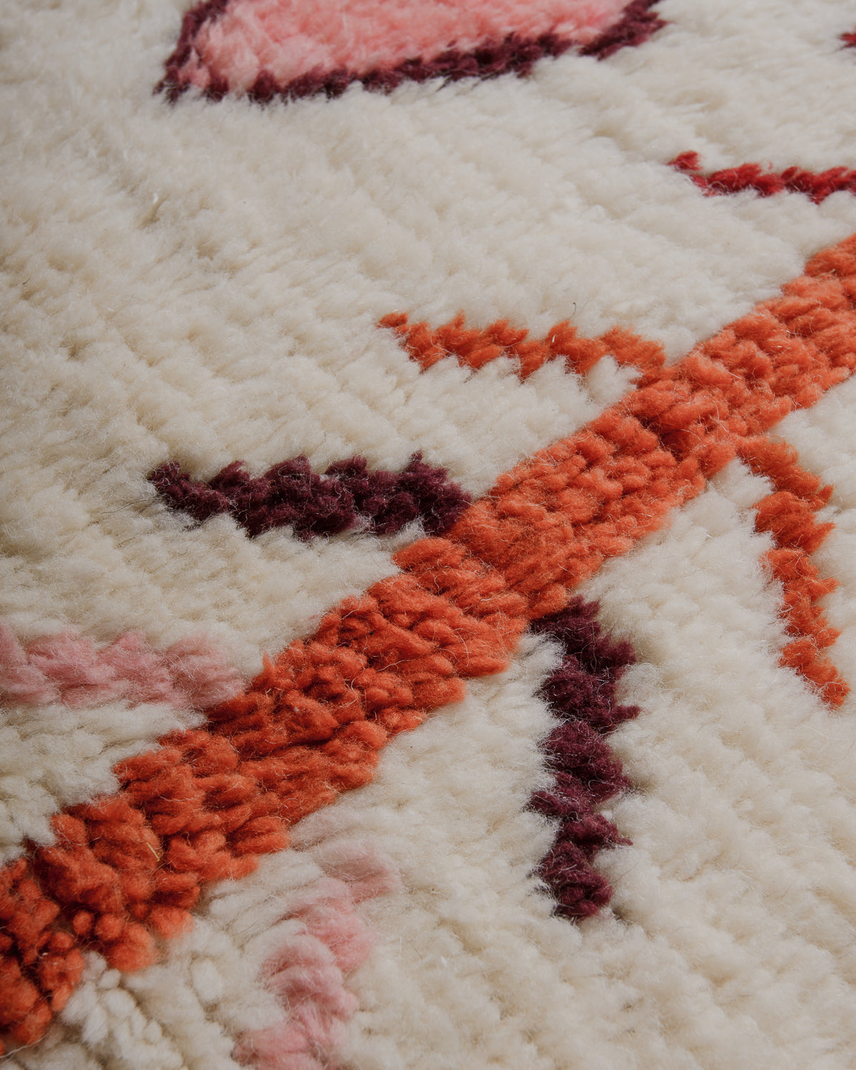 Texture of azilal rug made of soft sheep's wool in natural cream, rust, rose and burgundy.