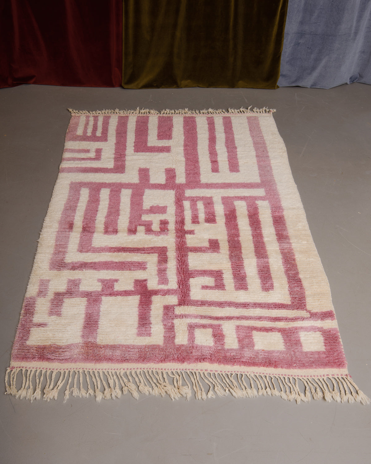 Azilal rug featuring colourful design on a grey floor in front of curtains.
