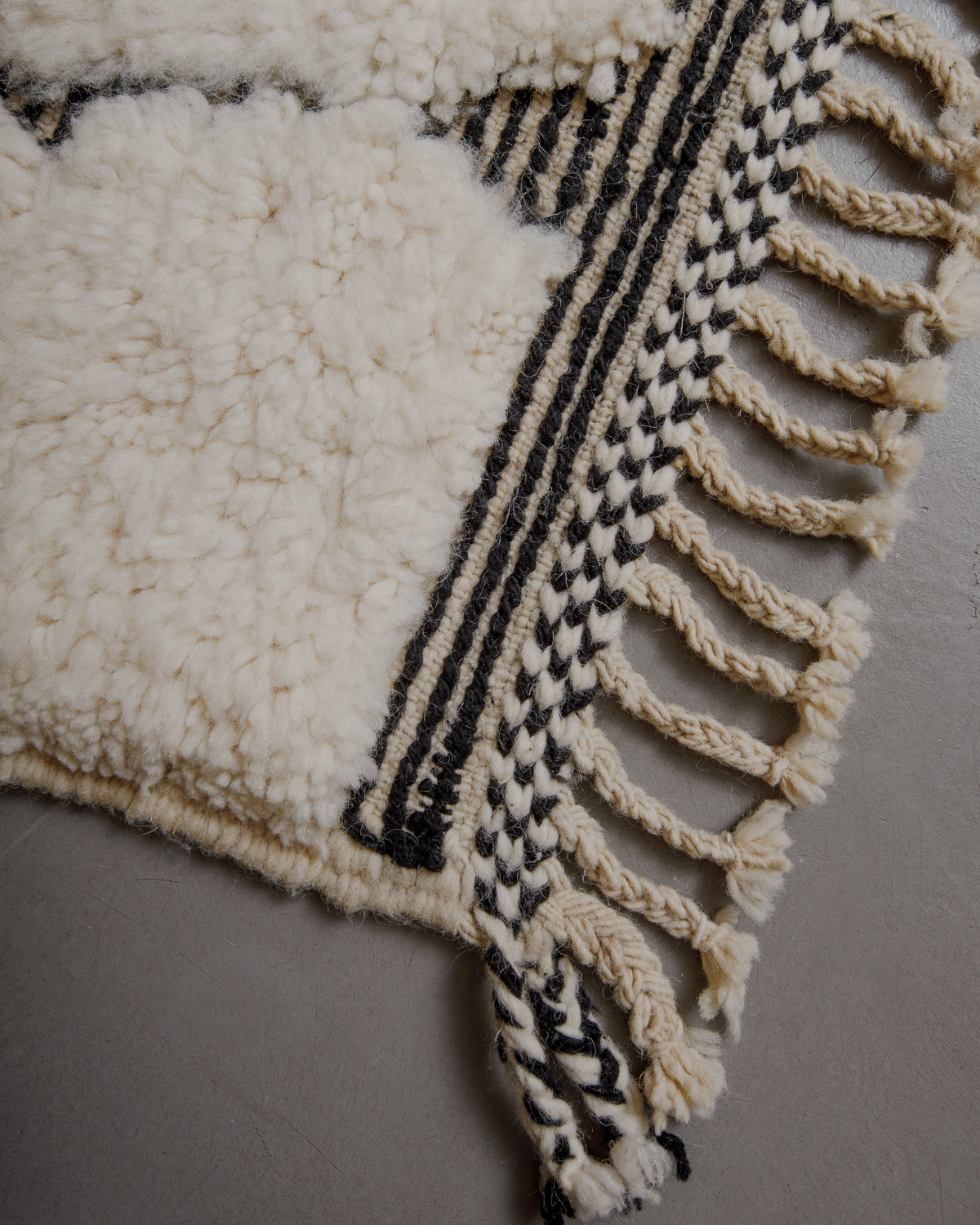 Edge of cream beniourain rug with natural wool tassels and black and white pattern along the edge.