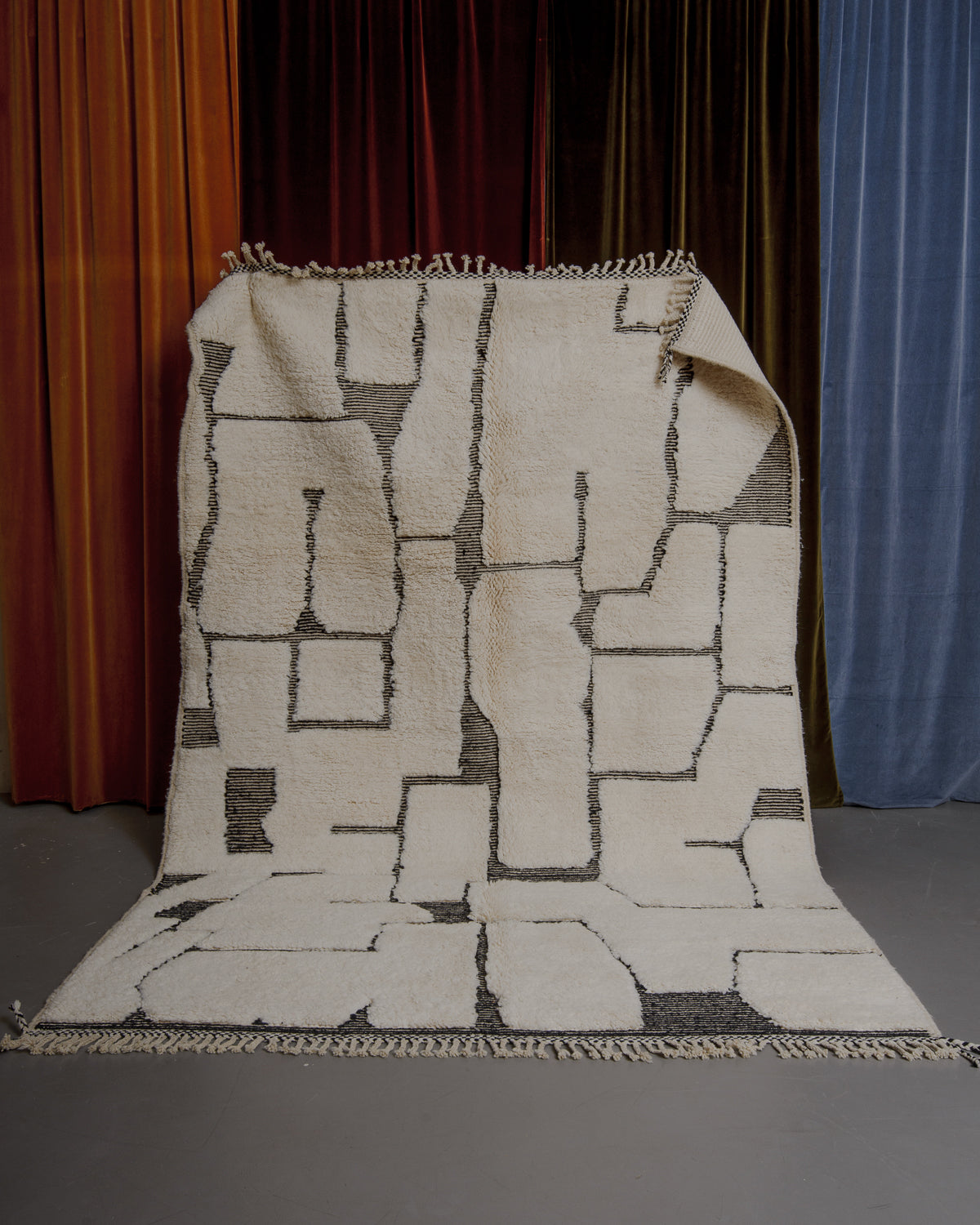 Cream and black Berberlin Beniourain rug held up in front of velvet curtains.