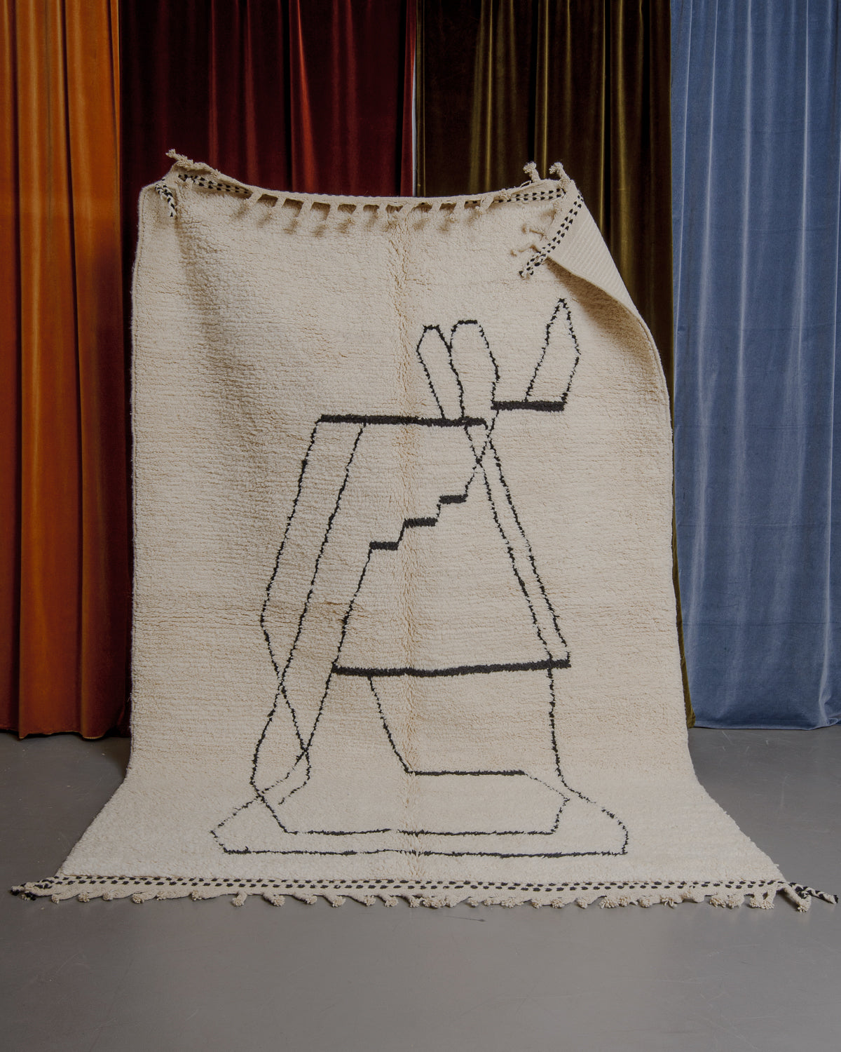 Berberlin Beniourain rug held in front of velvet curtains. 