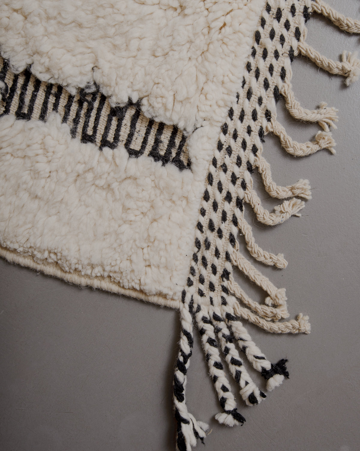 Edge of cream beniourain rug with natural wool tassels and black and white pattern along the edge.