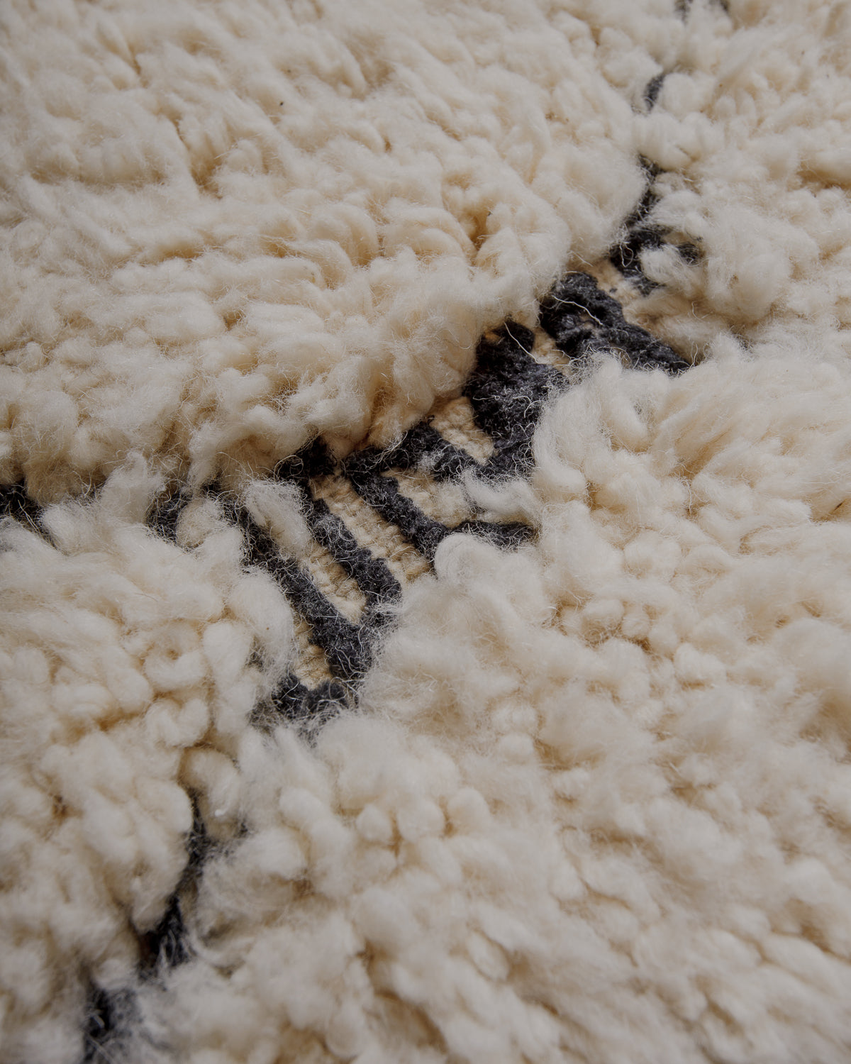 Surface of cream wool rug with pattern in embroidered black.
