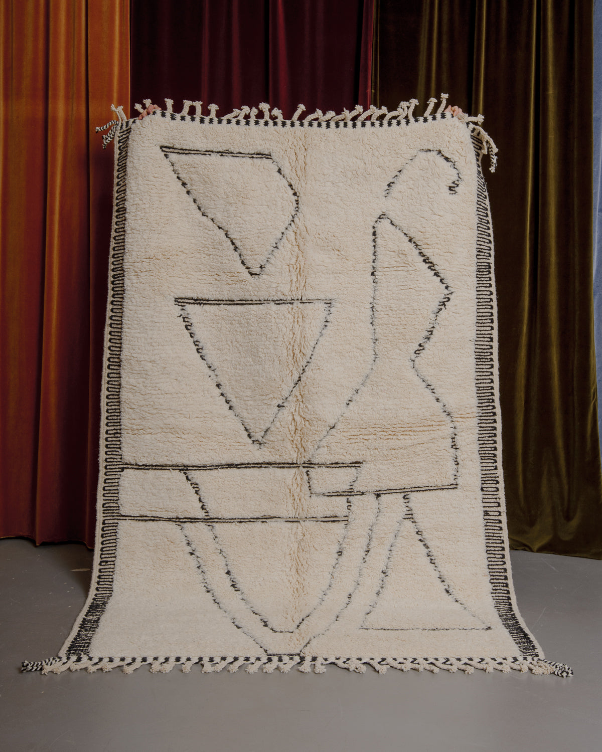 Cream and black Berberlin Beniourain rug held up in front of velvet curtains.