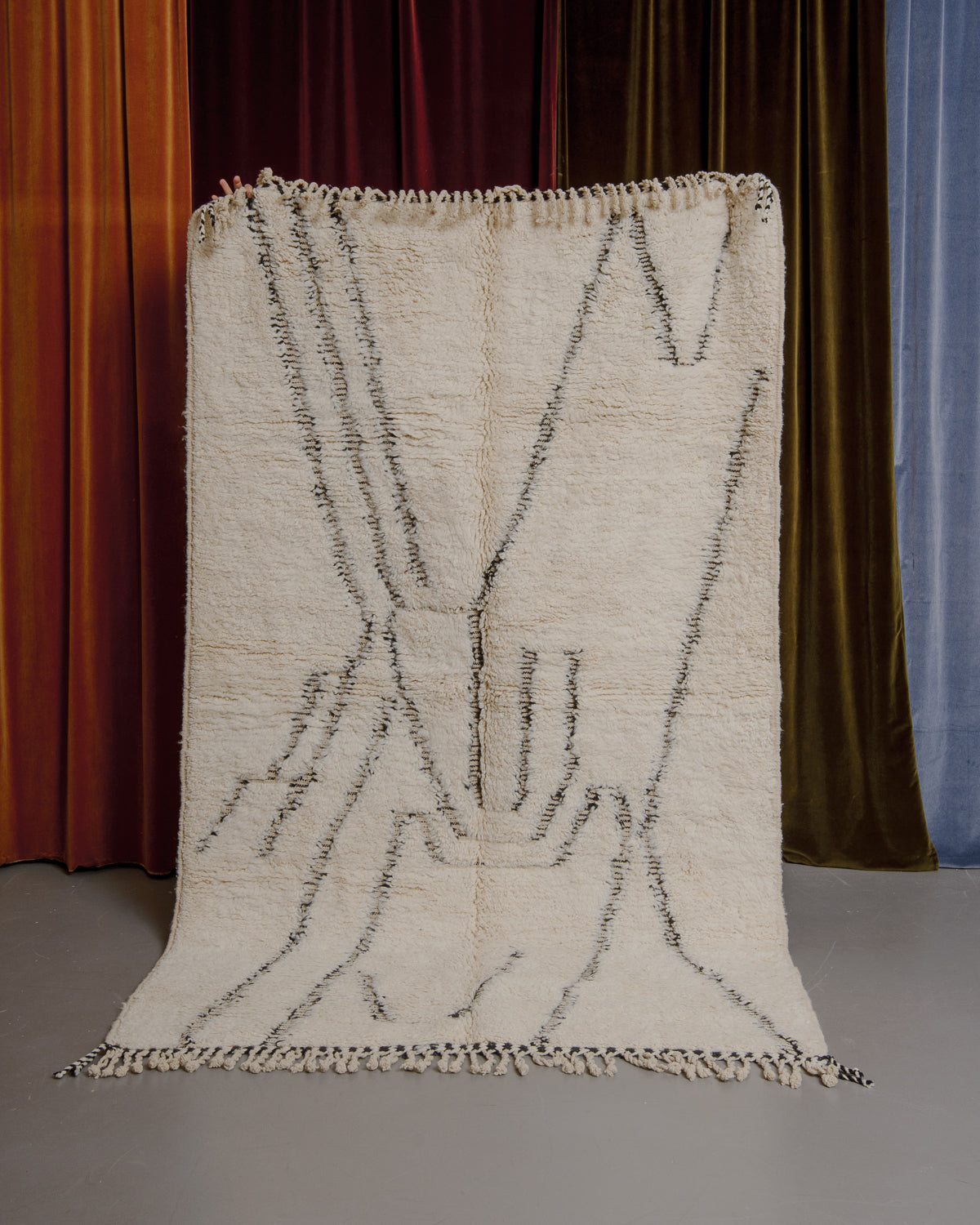 Cream and black Berberlin Beniourain rug held up in front of velvet curtains.