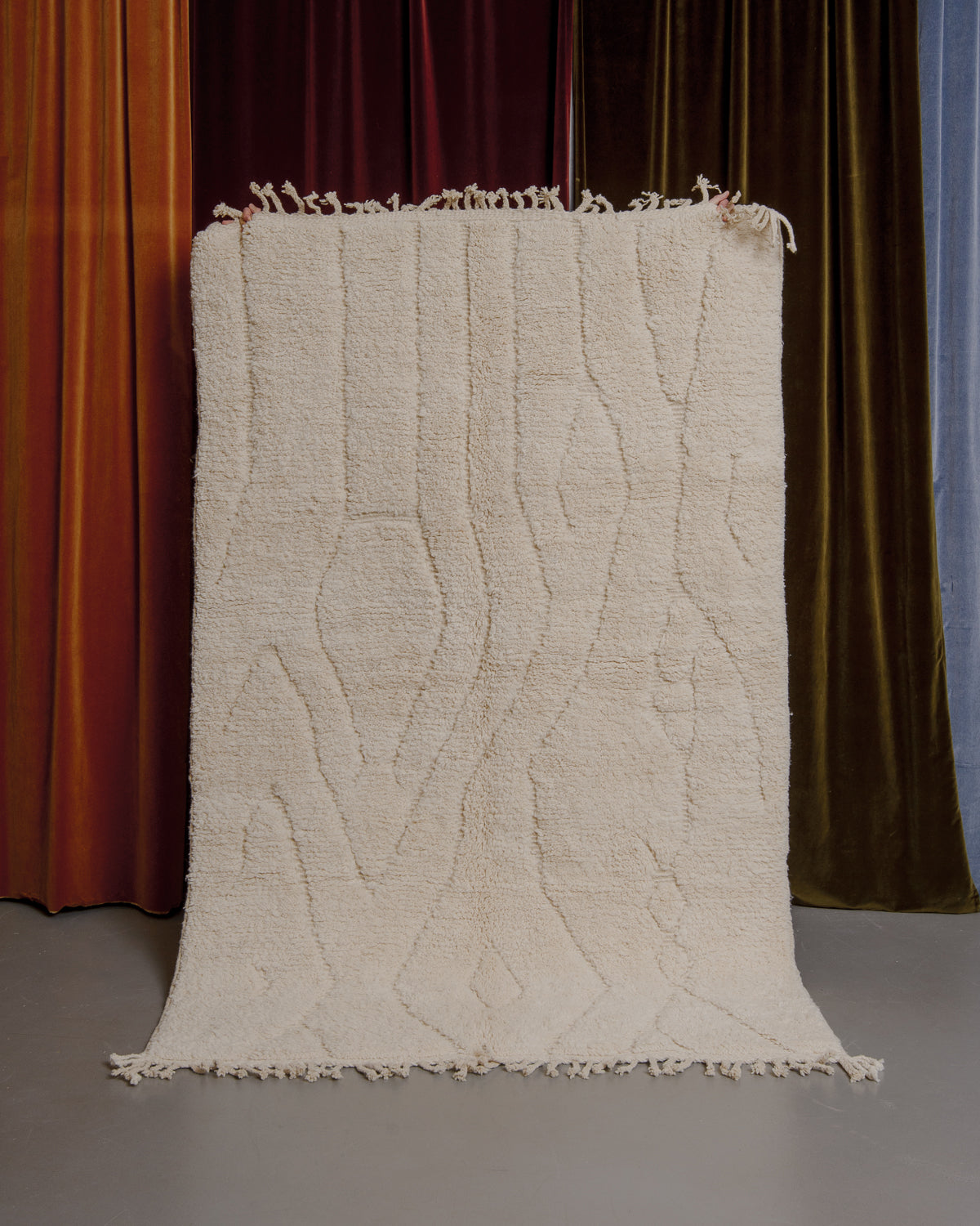 Cream Berberlin Beniourain rug held up in front of velvet curtains.
