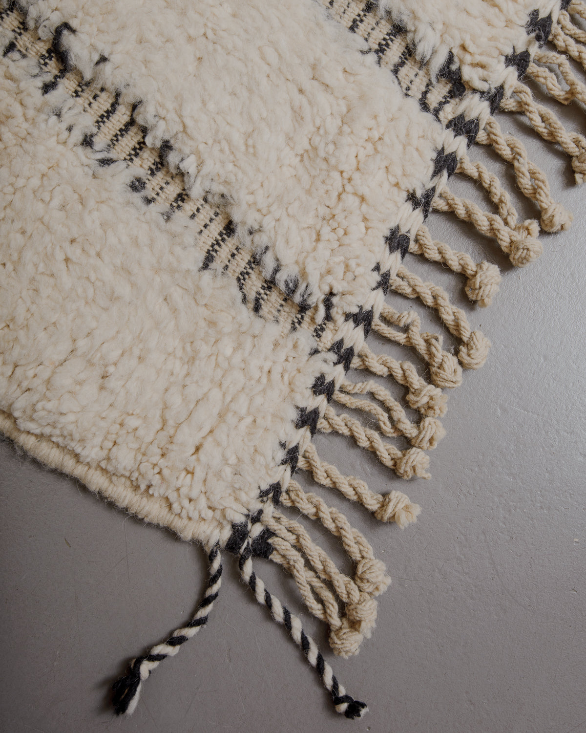 Edge of cream beniourain rug with natural wool tassels and black and white pattern along the edge.