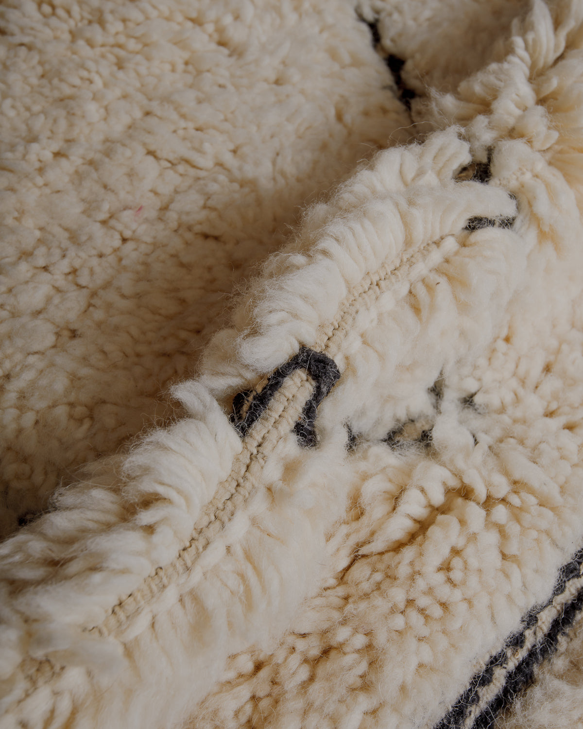 Fluffy cream wool pile with black embroidered lines .