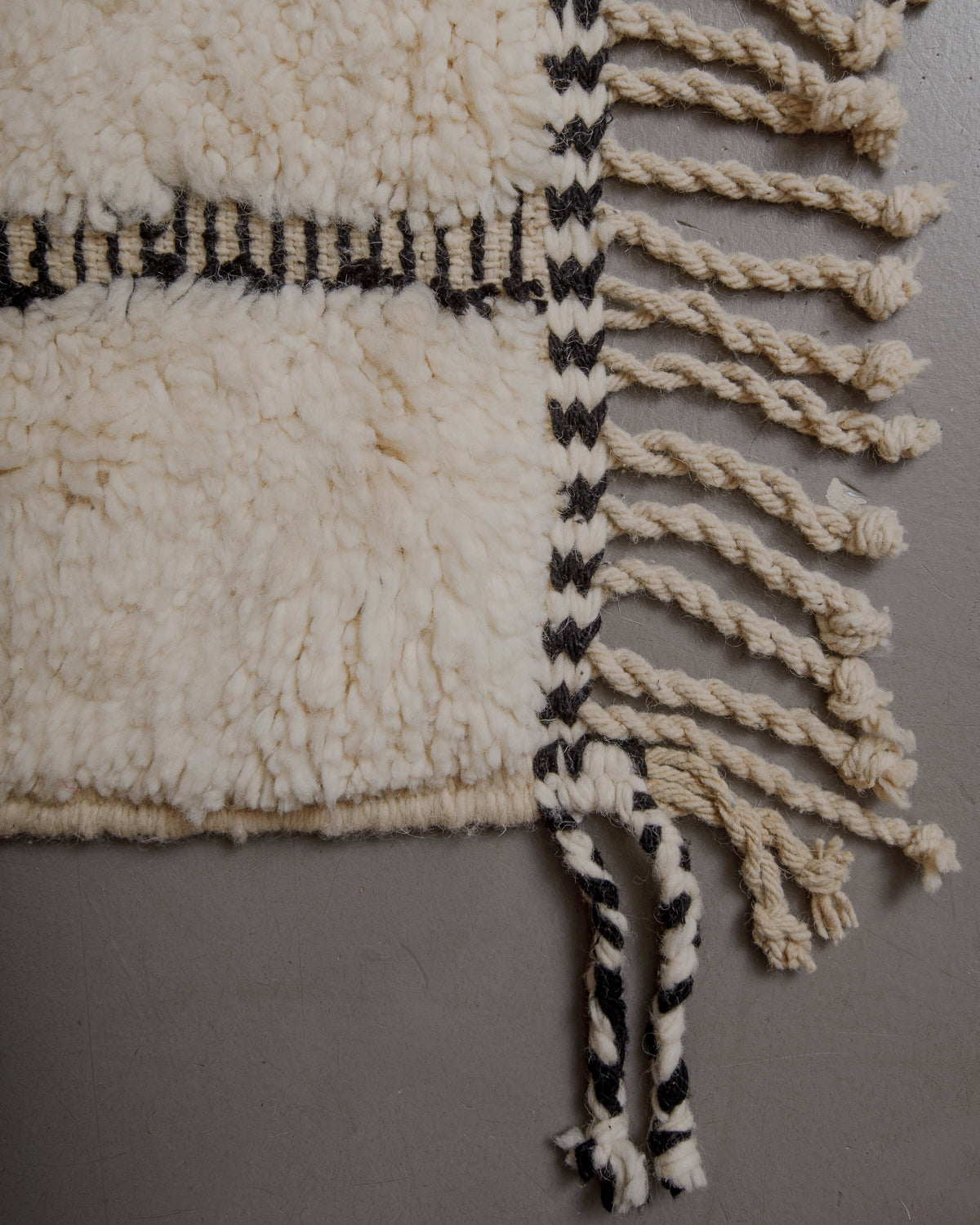 Edge of cream beniourain rug with natural wool tassels and black and white pattern along the edge.