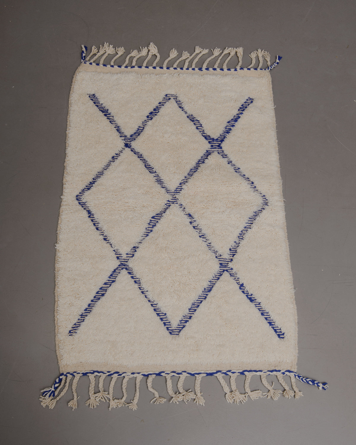 Wool rug with tassels on a grey floor.