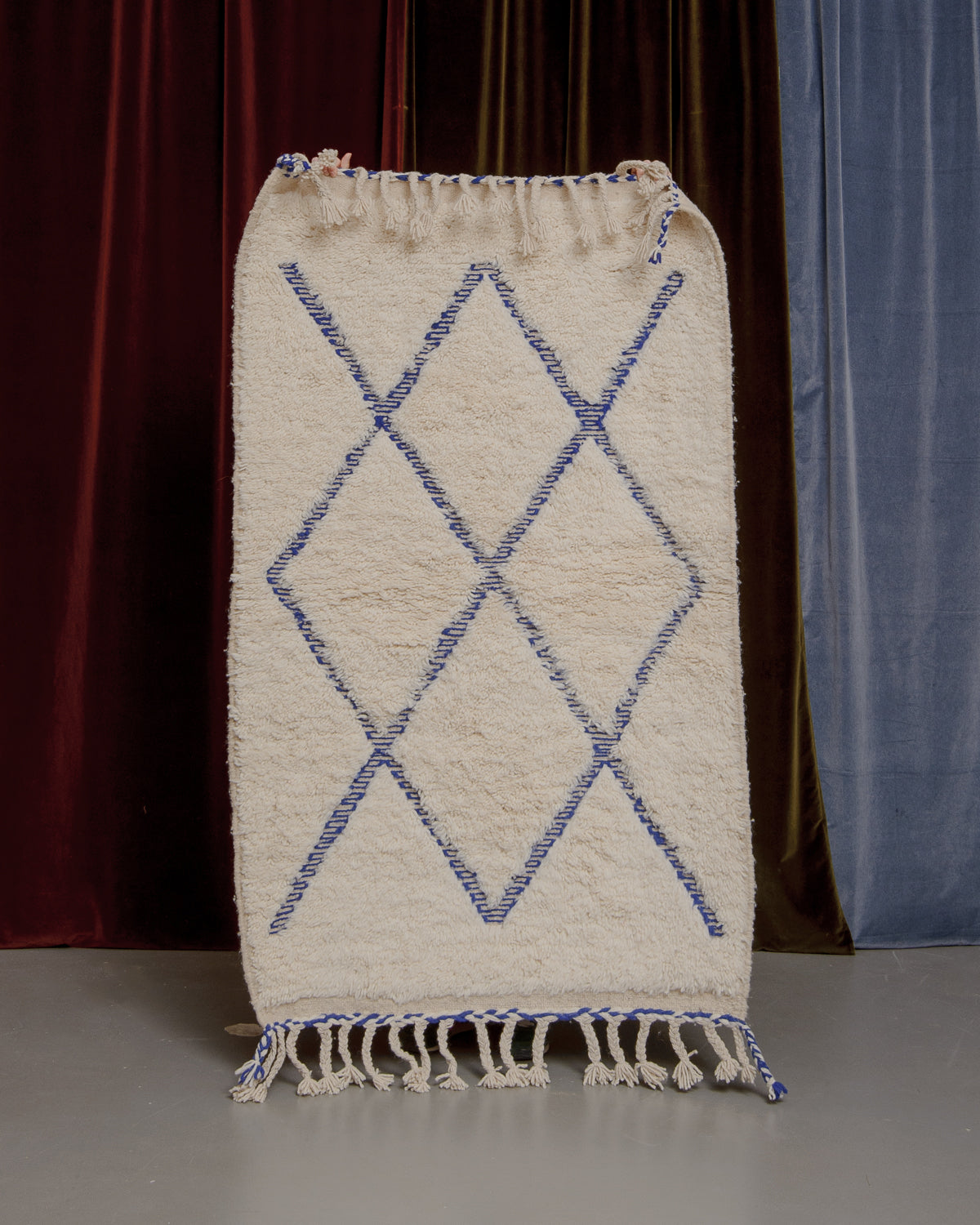 Berberlin Beniourain rug held up in front of a velvet curtain.