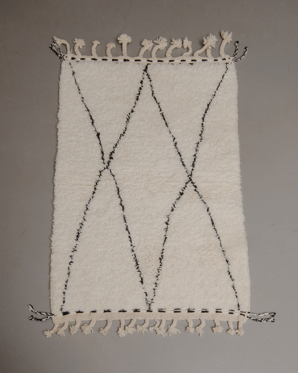 Wool rug with tassels on a grey floor.